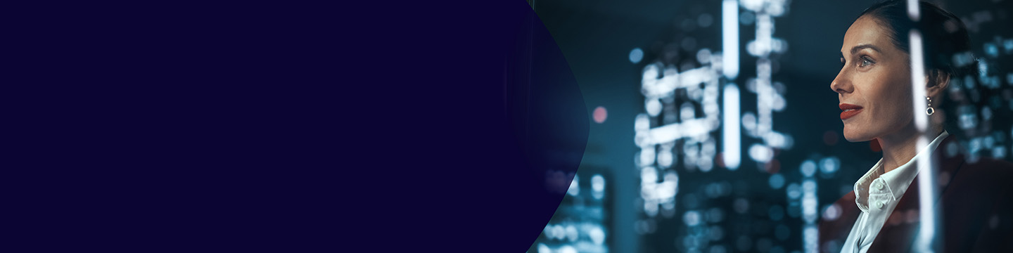 A professional woman standing indoors and looking at illuminated digital data displays, with bright city lights and reflections in the background.