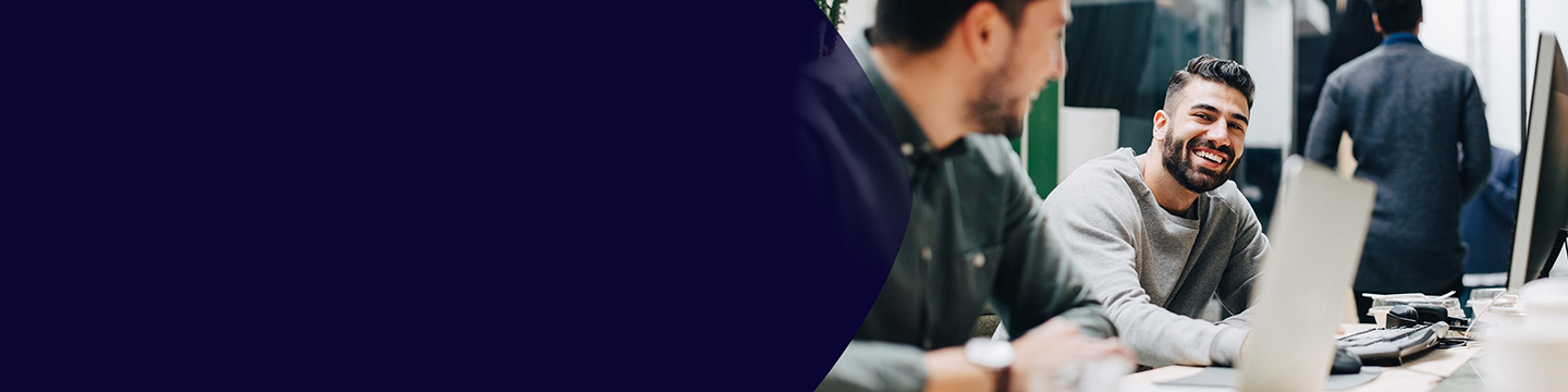 Emberek dolgoznak együtt egy modern irodai környezetben, laptopokkal felszerelt asztaloknál ülve, megbeszélésbe merülve.